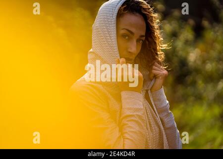 Sportswoman wearing hooded shirt staring while standing at park Stock Photo