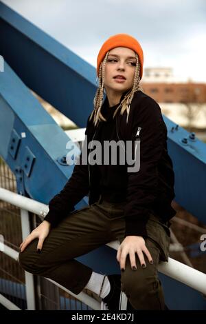 Thoughtful young woman with braided hair sitting on railing of bridge Stock Photo