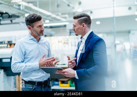 Male professionals with digital tablet having conversation while standing in factory Stock Photo