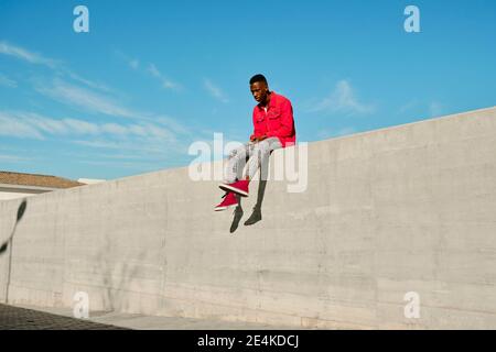 Young man in red jacket sitting on concrete wall Stock Photo