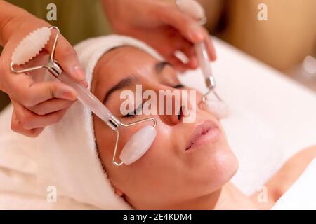 Young female customer receiving facial massage during treatment from beautician at spa