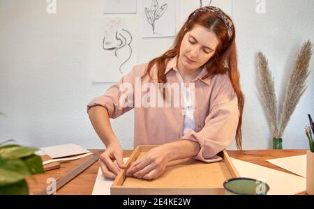 Female artist closing picture frame at desk while working at home