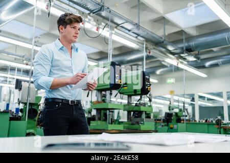 Young male entrepreneur with paper document looking away at factory Stock Photo