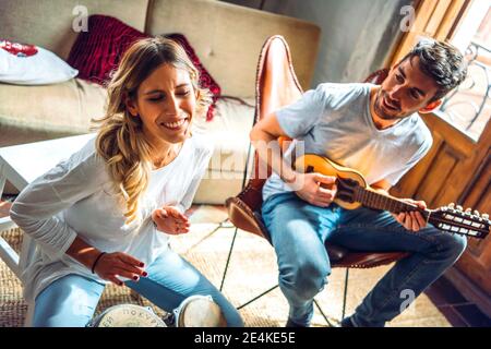 Happy young couple playing duet with drums and guitar in living room at home Stock Photo