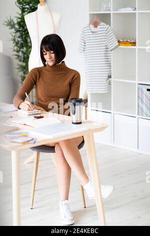 Female fashion designer working on new designs at desk in studio Stock Photo