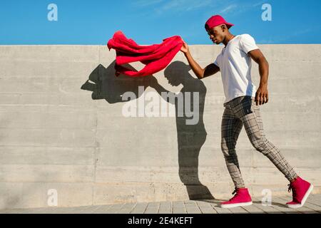 Young man holding red jacket and walking against concrete wall Stock Photo