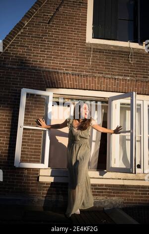 Cheerful woman with arms outstretched screaming while standing by window outside house Stock Photo