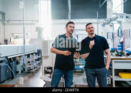 Male technicians with file document discussing at factory Stock Photo