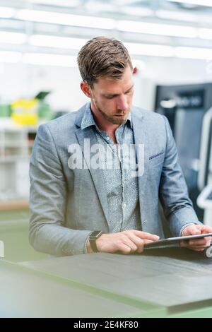Businessman in suit working on digital tablet while standing in factory Stock Photo