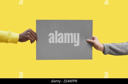 Graphic background image of two hands holding grey blank paper against pop yellow background, mock up, copy space Stock Photo