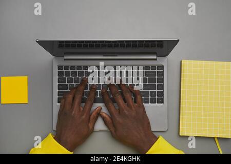 Graphic gray and yellow background of African-American male hands typing on laptop keyboard while working at desk, top down view, copy space Stock Photo