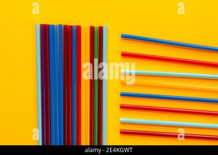On a yellow background, multicolored cocktail tubes lie, next to a bunch of vertical tubes lie horizontal Stock Photo