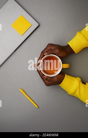 Minimal grey background of African-American male hands holding mug by laptop while working at desk, top down view, copy space Stock Photo