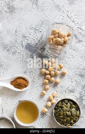 Overhead view of some granola ingredients with a laid glass jar full of hazelnuts, some ground cinnamon, seeds and a bowl of honey over a rustic grey Stock Photo
