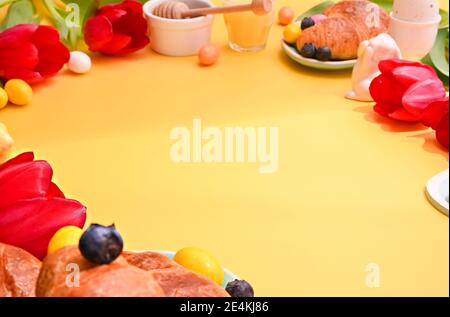 Beautiful Spring breakfast. Espresso coffee in bright cups, Easter chocolate eggs and red tulips on a yellow background. Copy space.  Stock Photo