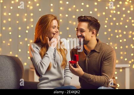 Happy young man making wonderful surprise for his girlfriend, giving her beautiful ring Stock Photo