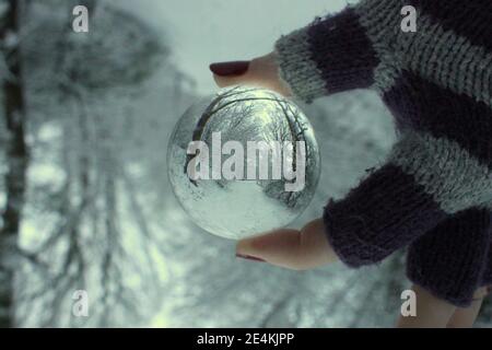 A photograph of a snowy winter landscape refracted in a lensball held by a female hand in a glove Stock Photo