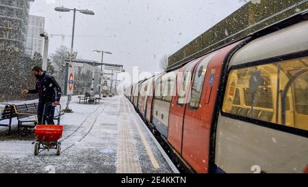 TfL worker hurriedly applies grit salt to train platform at Colindale Tube Station whilst it snows on 24th January 2021. Transport for London are unprepared for bad weather on the London underground network despite Met Office weather warnings being in place for heavy snowfall. Colindale, London. UK Weather. Stock Photo