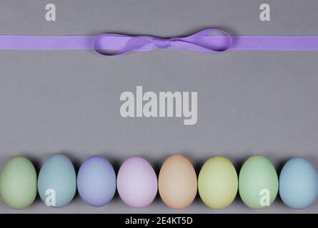 Easter theme layout with a row of pastel colored eggs across the bottom in blue, green, yellow, orange, pink and purple and a purple ribbon tied in a Stock Photo