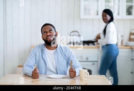 Impatient hungry black husband waiting for dinner with empty plate, looking bored Stock Photo
