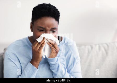 Sick black woman sneezing, holding tissue paper Stock Photo