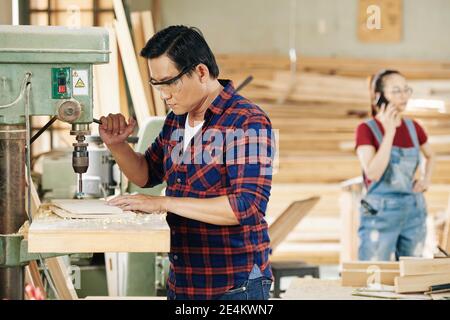 Carpenter working with carpenter setting milling cutter machine when making holes in wood planks in carpentry workshop Stock Photo
