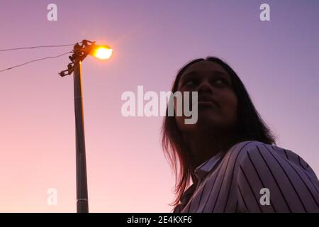 Cape Town, South Africa - 20-02-2020 Creative and hazy purple sunset and street lamp. Stylish young woman silhouetted in foreground. Stock Photo