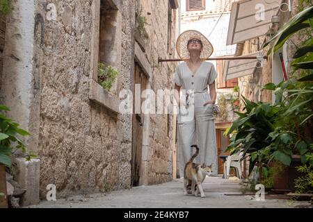 Beautiful blonde young female traveler wearing straw sun hat sightseeing and enjoying summer vacation in an old traditional costal town at Adriatic Stock Photo