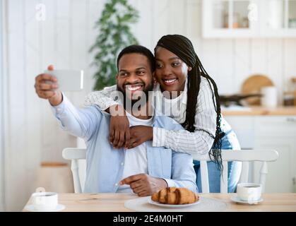 Romantic African Couple Taking Selfie On Smartphone While Having Breakfast In Kitchen Stock Photo