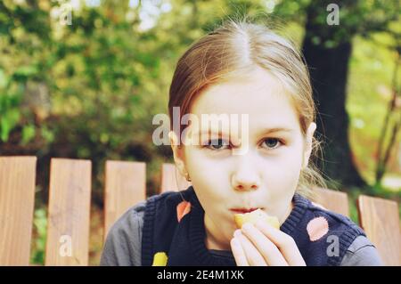 Young white European girl (child, kid) eat a biscuit in the park Stock Photo