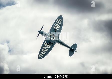 Thank U You NHS WW2 Second World War Spitfire aeroplane flying over Nottingham hospital during Coronavirus Covid 19 pandemic stormy sky clouds look up Stock Photo