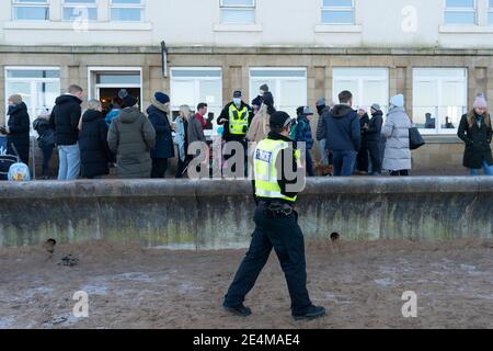 Portobello, Scotland, UK. 24 January 2021. Large numbers of members of the public at Portobello beach and promenade on sunny Sunday afternoon during lockdown. While most people observed social distancing groups of people formed at some of the cafes offering takeaway food and drinks. Police patrols spoke to public sitting down and in groups at cafes to ask them to move on. Pic; Police talk to members of the public gathered outside cafe and ask them to move on. Iain Masterton/Alamy Live News Stock Photo