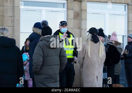 Portobello, Scotland, UK. 24 January 2021. Large numbers of members of the public at Portobello beach and promenade on sunny Sunday afternoon during lockdown. While most people observed social distancing groups of people formed at some of the cafes offering takeaway food and drinks. Police patrols spoke to public sitting down and in groups at cafes to ask them to move on. Pic; Police talk to members of the public gathered outside cafe and ask them to move on. Iain Masterton/Alamy Live News Stock Photo