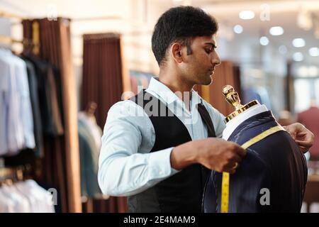 Concentrated young Indian tailor measuring bespoke jacket shoulders with tape measure Stock Photo