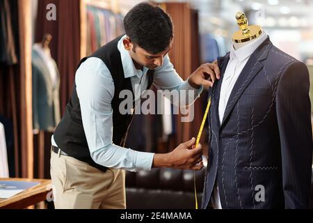 Creative young tailor measuring bespoke jacket on mannequin he is working on Stock Photo