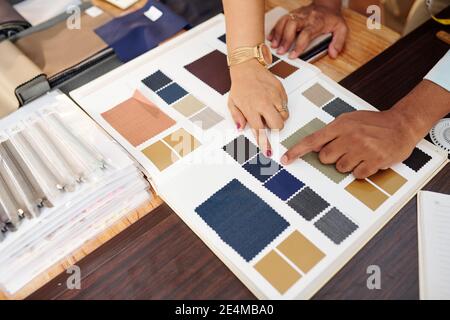 Hands of tailor and client choosing fabric from catalog for making bespoke suit Stock Photo