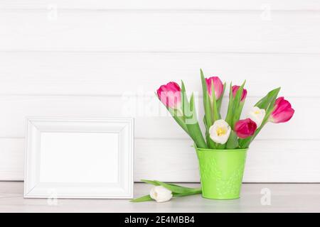 Blank white photo frame with tulip flower bouquet on the table near the wall. Spring mockup background Stock Photo