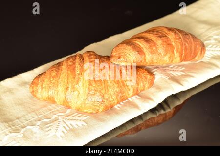 Two whole fragrant sweet fresh crunchy croissants on a black background lie on a linen napkin. Stock Photo