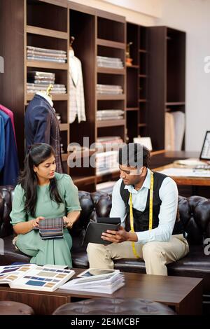 Tailor showing fabric catalog to female client when they are meeting in atelier to discuss bespoke suit Stock Photo