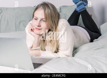 A  woman with her legs raised slightly in front of her laptop lying on the bed. Working from home in quarantine lockdown. Social distancing Self Isola Stock Photo