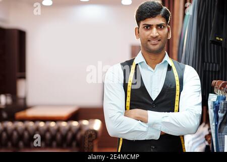 Portrait of young handsome Indian tailor with measuting tape standing with arms folded and looking at camera Stock Photo