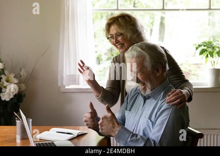 Overjoyed mature man and woman waving hands, chatting online Stock Photo