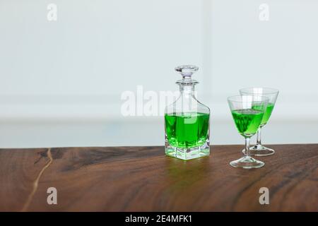 A green poisonous drink in a small bottle and two cocktail glasses on a table. A strong venomous chemical mixture. Stock Photo