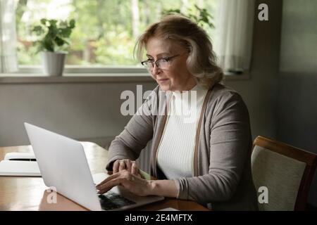 Confident mature woman wearing glasses using laptop, browsing apps Stock Photo