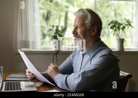 Focused elderly man reading letter, checking documents, working with correspondence Stock Photo