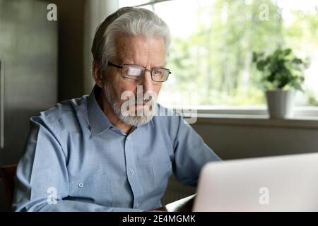 Close up focused mature man wearing glasses using laptop Stock Photo