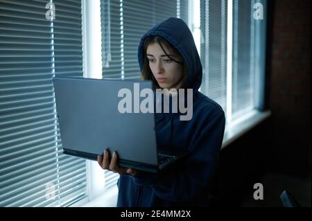 Female internet hacker in hood works on laptop Stock Photo