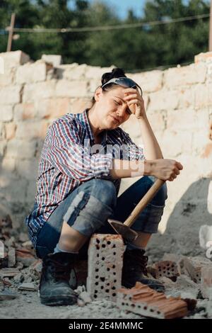 Female constructer holding a hammer and wiping sweat off her forehead Stock Photo