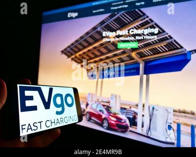 Holding mobile phone with logo of EVgo Services LLC, a provider of eletric vehicle (EV) charging network in US. Focus on left part of phone display. Stock Photo