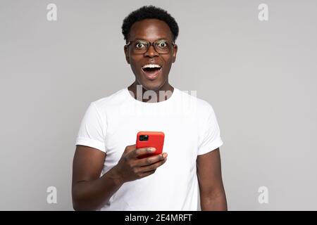 Happy African millennial man in glasses wear white t-shirt, holding mobile phone, isolated on studio Stock Photo